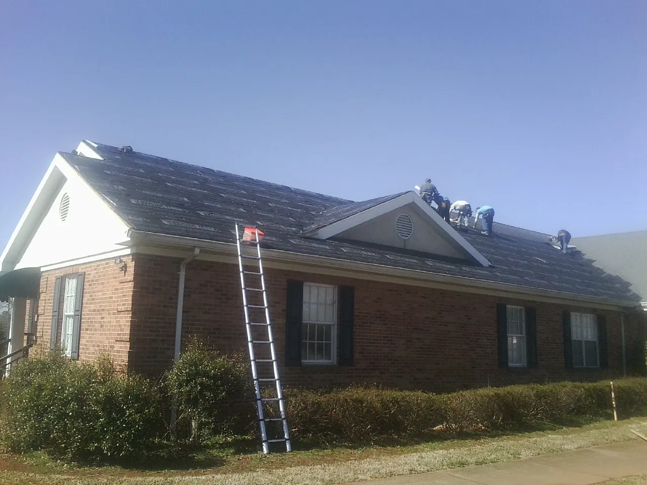 Crew tearing shingles off a brick ranch roof with a ladder set — Metal Roof Repair work by our crew in North Kingstown