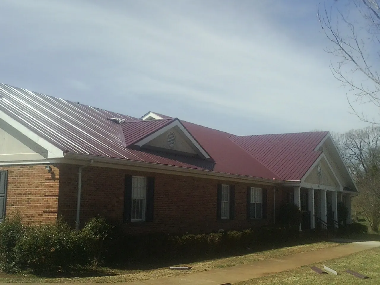 Red metal roof with gabled entries on a long brick building, from a Hail Damage Roof Repair job in North Kingstown