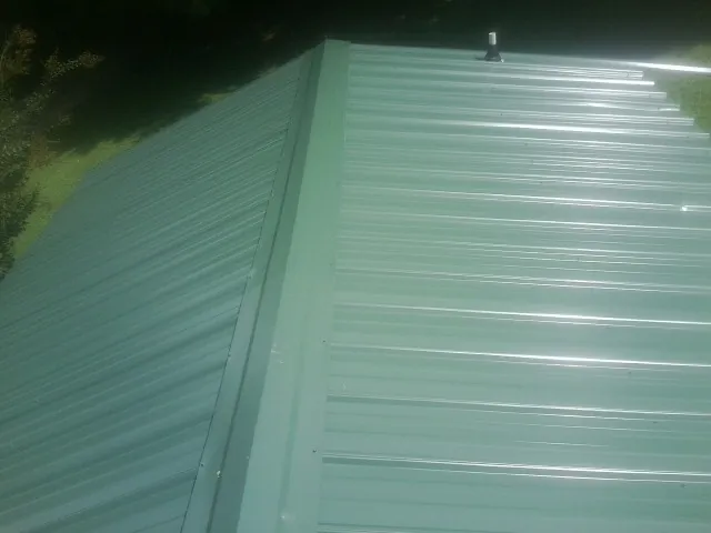 New green metal panels meeting at the ridge of a roof — Flat Roof Repair work by our crew in North Kingstown