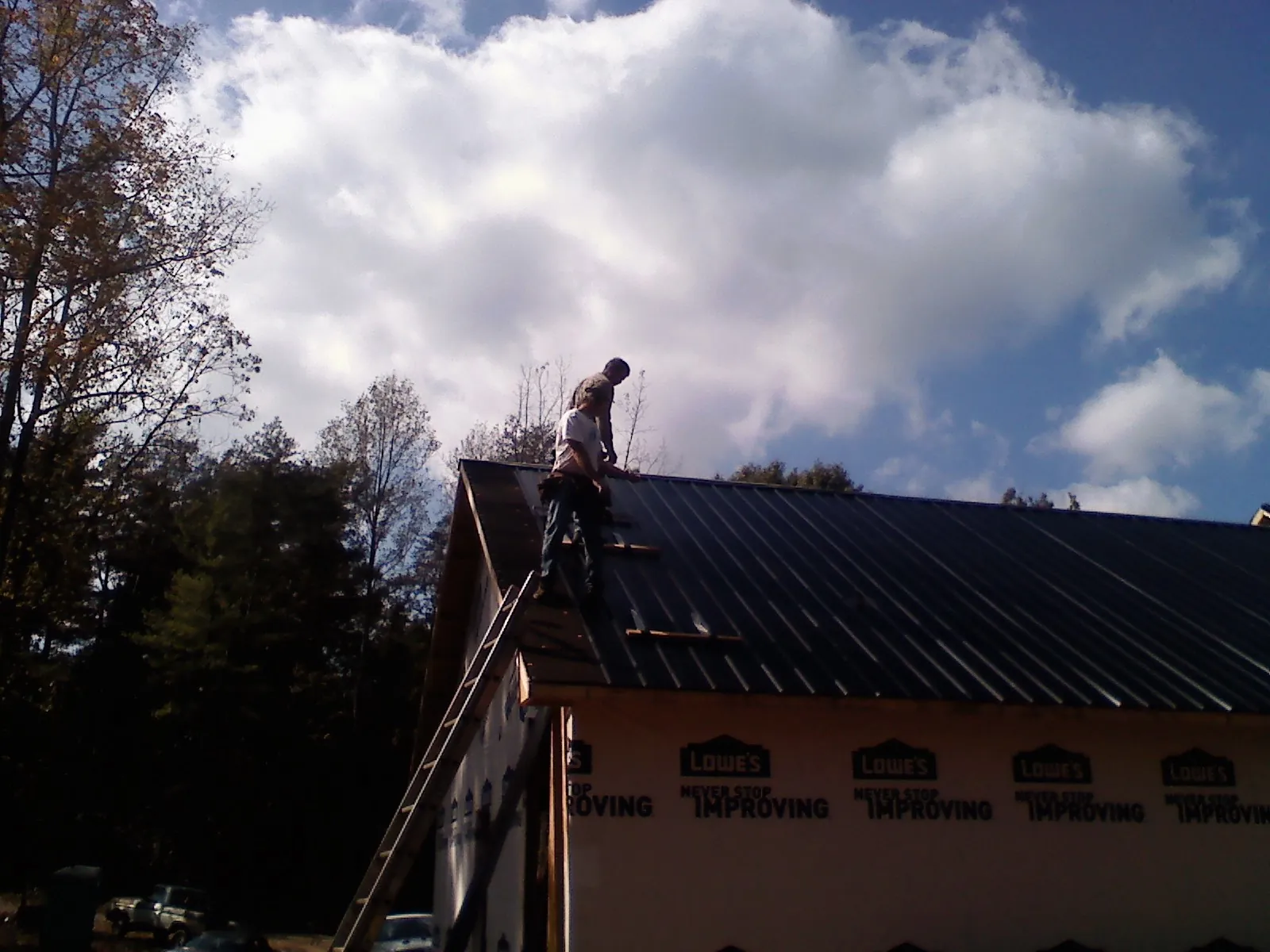 Roofer fastening dark metal panels high against a cloudy sky, from a Roof Inspection job in North Kingstown
