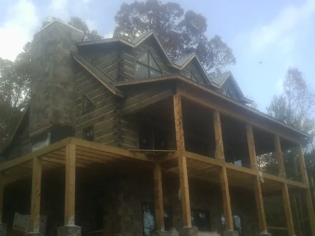Stone chimney and dormers on a large log home with a timber porch in North Kingstown
