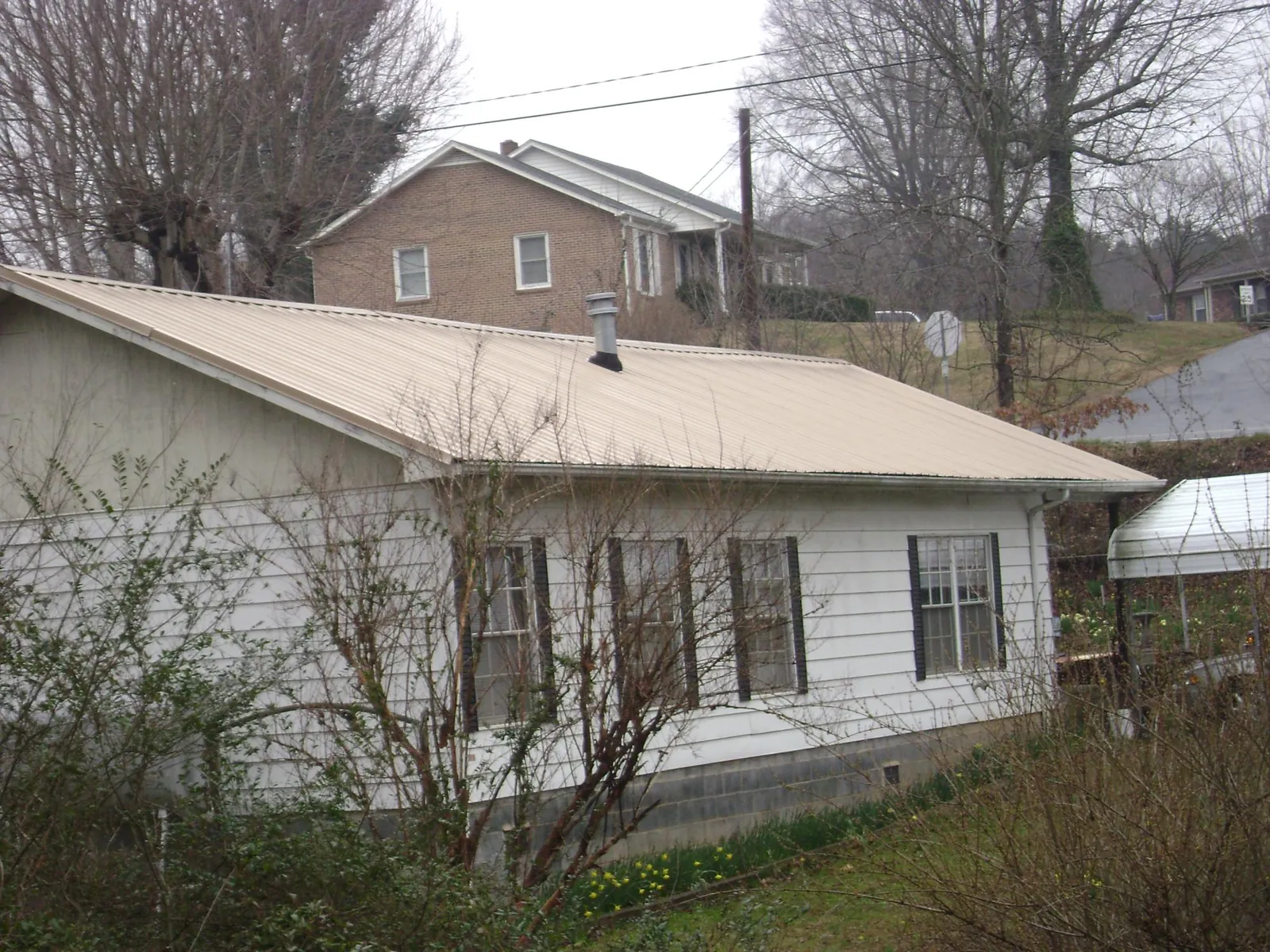 Tan metal roof on a white sided house set into a hillside — Commercial Roofing by Roofing Brothers in North Kingstown